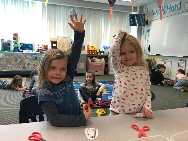 Two preschool girls raising their hands
